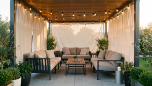 Terrasse couverte moderne et chaleureuse avec mobilier extérieur, protections latérales et éclairage doux par temps doux.