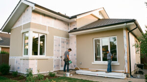 Maison rénovée avec isolation extérieure visible, fenêtres modernes et deux artisans travaillant dehors sous une lumière douce.