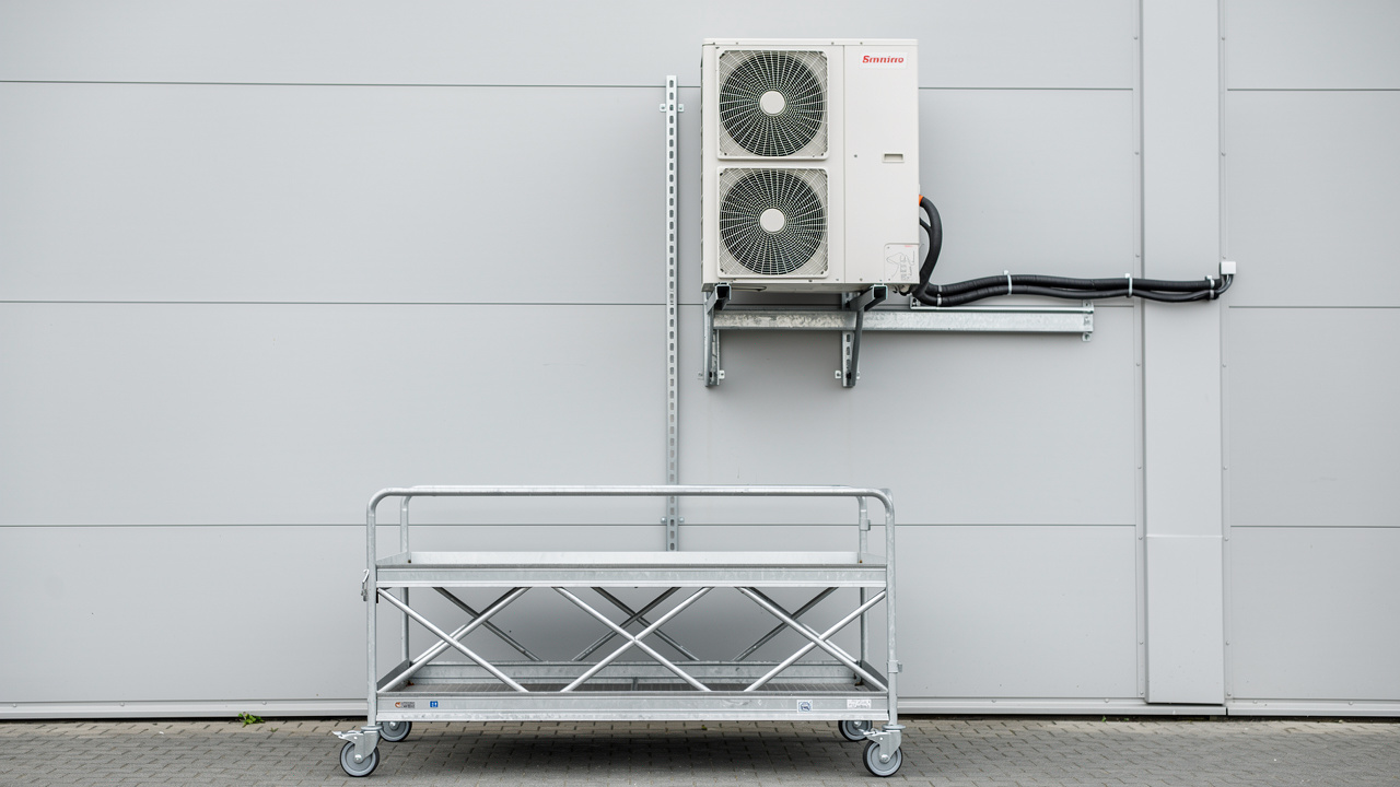 Groupe extérieur de pompe à chaleur air-air fixé sur une façade avec consoles métalliques, supports anti-vibratiles et plateforme roulante sécurisée.